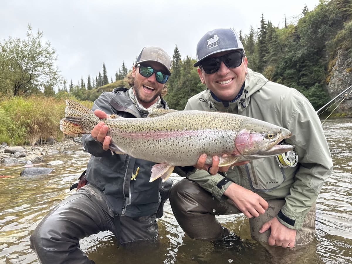 Two anglers on a river holding a rainbow trout before release