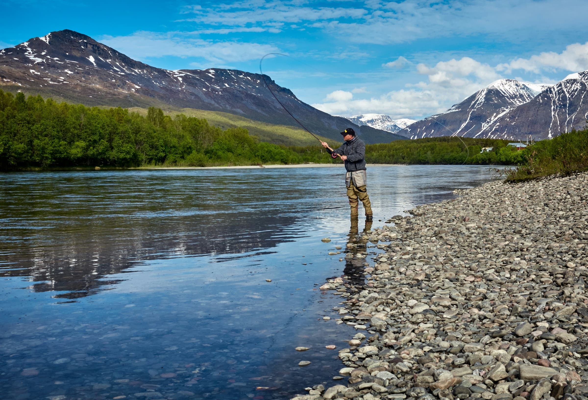 An angler casting a fly line on a wide mountain river.